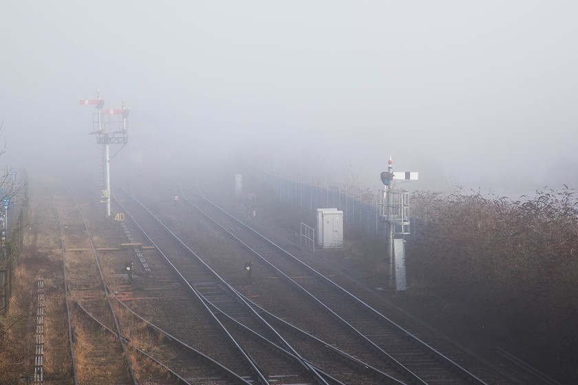 Signals, Droitwich Spa 
 Some lower quadrant Western Region signals sit in the fog at Droitwich. In this view, taken from Acre Lane Bridge, the out of use sidings can be seen to the left. Behind the home signal to the right was the old coal yard, this was a site that has featured in many pictures taken from this bridge. The signal box cannot be seen in this image because of the fog, it's behind the down bracket signal. 
 Keywords: Droitwich Spa semaphores