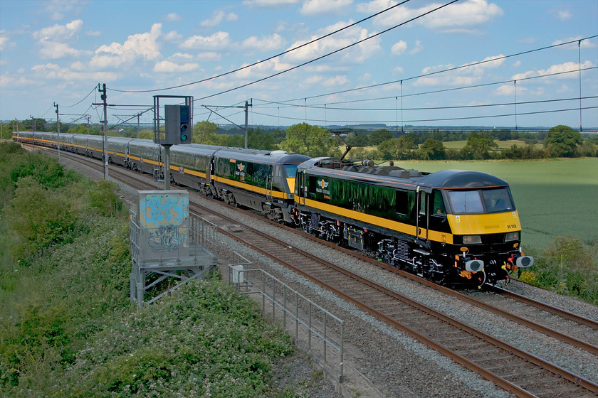 90029, 82200, 82227 & 90026, 09.37 Widnes Transport Tech-Wembley Yard (5Z90, 8L), Milton crossing 
 Despite being owned by Arriva, Grand Central has a very distinctive corporate image and one nothing like any other train operating company with a philosophy to match. At one time during the recent COVID-19 pandemic, it was looking likely that its future operating trains may have come to an end with a complete shutdown of its services on the ECML and all staff furloughed. All this was just as it was about to launch its WCML operations in and out of Euston to great fanfare. This launch has now been put back to 2021 with driver training still to start as Grand Central attempts to resurrect its services and build its business again. In preparation for training and for services, two cut down sets of former LNER Mk.IVs, two DVTs and a second Class 90 were sent to Alstoms Technology Centre in Widnes to be outshopped in GC's smart black and gold livery. Here the two sets pass Milton Crossing on the Weedon loop just north of Roade cutting as the 5Z90 09.37 Widnes to Wembley Yard. There were an awful lot of photographers at this location, in fact, the most I have seen here since the end of the Class 87 Virgin evening commuter train but we were all denied a decent photograph as the sun went in just ten seconds before it arrived - the rear of the train is still in full sun! This particular image took me a considerable amount of time in Photoshop to resurrect it from a hopelessly dark subject and overexposed background but even so it is still very disappointing but, given the subject matter, it has made the cut! The train is being led by 90029 with the full list of stock as follows: 82200, 11320, 10321, 12326, 12477, 12224, 82227, 11321, 10330, 12323, 12461, 12222 and on the rear is 90026. 
 Keywords: 90029 82200,82227 90026 09.37 Widnes Transport Tech-Wembley Yard 5Z90 Milton crossing GC Grand Central DVT