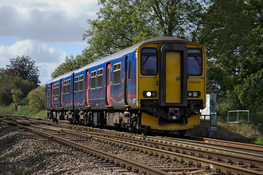 150249, GW 11.10 Weymouth-Bristol Temple Meads (2V90), Blatchbridge Junction 
 A picture that perfectly illustrates why I find this time of year a contradiction. Whilst, on the one hand, I feel somewhat down about the end of summer with the ever-shortening days (do I suffer from SAD?) the lighting for photography is absolutely superb. With the sun much lower in the sky, even in the early afternoon, it is able to illuminate parts of the underframe of 150249 as it passes Blatchbridge Junction. The Sprinter is about to diverge to its left off the mainline and head into Frome whilst working the 11.19 Weymouth to Bristol Temple Meads. Blatchbridge Junction signal box used to be located on the right approximately level with the rear coach of the train. The photograph is taken from the security of a cage at a foot crossing. 
 Keywords: 150249 11.10 Weymouth-Bristol Temple Meads 2V90 Blatchbridge Junction FGW First Great Western