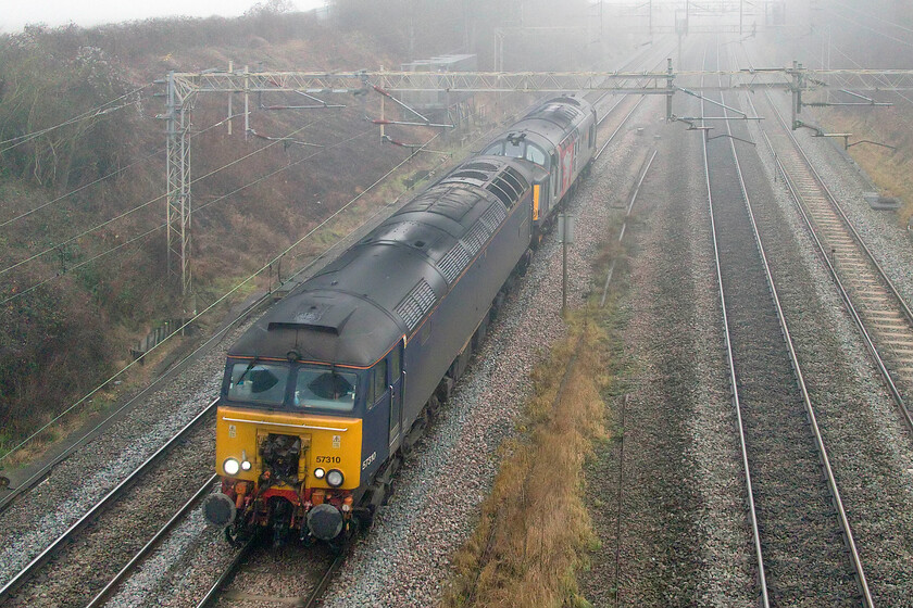 57310 & 37611, 12.42 Wembley Yard-Derby RVEL (0M57, 9E), Victoria bridge 
 57310 'Pride of Cumbria' leads 37611'Pegasus' through the fog at Victoria bridge just south of the Northamptonshire village of Roade. I am not at all sure as to the purpose of the move, running as 0M57, but it did have several posts on the internet so I was able to monitor its progress. I almost missed the passing of the two locomotives running as the 12.42 Wembley Yard to Derby RVEL as it was pretty silent and emerged from the fog catching me out with the camera not ready but I still just managed this photograph. 
 Keywords: 57310 37611 12.42 Wembley Yard-Derby RVEL 0M57 Victoria bridge Rail Operations Group Pride of Cumbria Pegasus