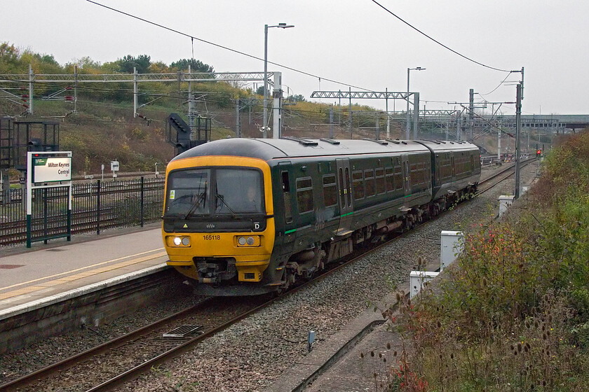 165118, 09.50 Wolverton Centre Sidings-Reading TMD (5Q74, 5E), Milton Keynes station 
 Having been receiving attention at Wolverton Works by Gemini Rail 165118 returns to its western haunts as the 09.50 Wolverton Centre Sidings to Reading TMD. The train is seen passing MIlton Keynes station in very poor lighting. As an indication of how poor it is notice the illumination of the running-in sign glowing nicely even though it has just past 10.00! 
 Keywords: 165118 09.50 Wolverton Centre Sidings-Reading TMD 5Q74 Milton Keynes station GWR Turbo