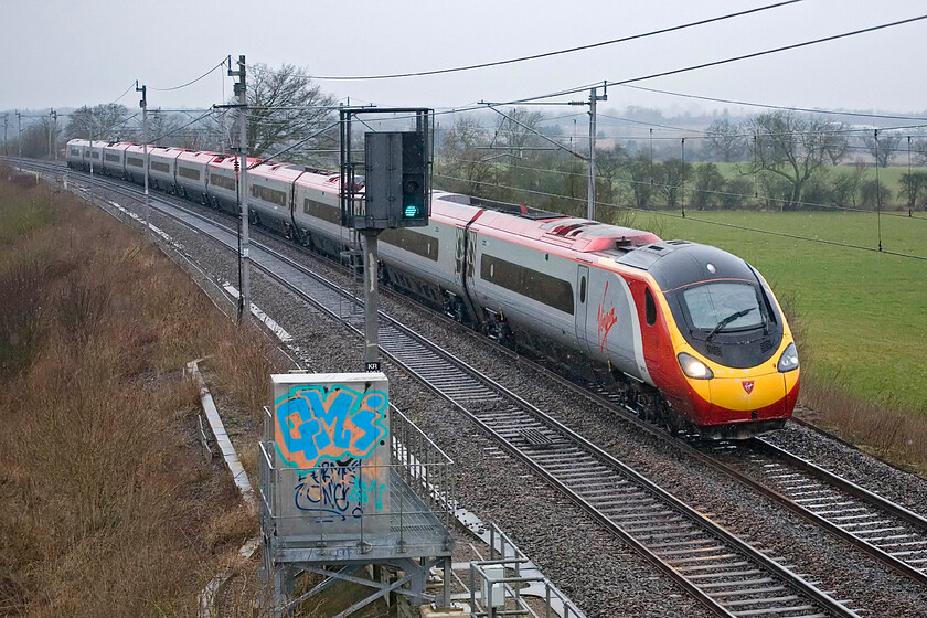 Class 390, VT 06.35 Manchester Piccadilly-London Euston, Milton Crossing 
 A Virgin Pendolino heads south towards London at Milon crossing between Road and Blisworth working the 06.35 Manchester-Euston service. Whilst some call it graffiti art I see it more as wanton vandalism of the relay box seen in the foreground. 
 Keywords: Class 390 06.35 Manchester Piccadilly-London Euston Milton Crossing Virgin West Coast Pendolino