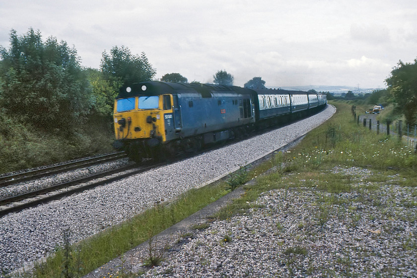 50041, 06.50 Plymouth-London Paddington, Burlescombe ST071168 
 On such a dull morning taking photographs on the Zenith camera (that I had started to re-use again) was a difficult proposition with its slow lens and poor maximum shutter speed. However, this photograph showing 50041 'Bulwark' leading the 06.50 Plymouth to Paddington is interesting in that it shows our camping spot as can be witnessed by UAM the orange Mini. This spot is near the village of Burlescombe with the track to the right where we were camping being the course of the former Burlescombe Tramway that linked the mainline with Westleigh Quarry a short distance to the north. 
 Keywords: 50041 Bulwark 06.50 Plymouth-London Paddington, Burlescombe ST071168