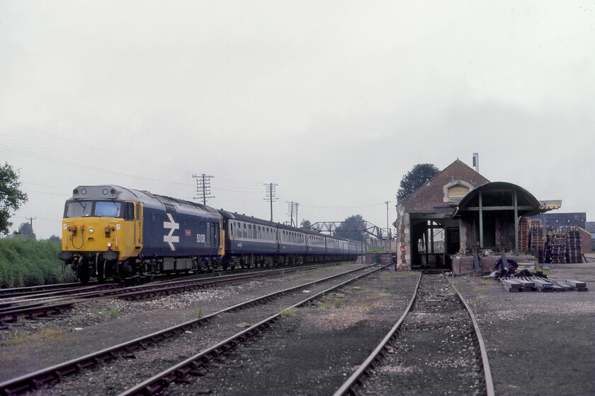 50038, 07.38 Exeter St. David's-London Waterloo (1O06), Whimple goods yard 
 50038 'Formidable' leads the 07.38 Exeter St. David's to Waterloo service away from the small station at Whimple in Devon. 50038 still looks smart in its large logo livery applied during its six-month refurbishment being released back into traffic in November 1980. The photograph is deliberately framed off centre to also include the delightful Southern Railway goods shed that is remarkably intact complete with its timber canopy. The yard, whilst much diminished in size, still contained a couple of wagons and appeared to be in use witnessed by the pile of pallets. 
 Keywords: 50038 07.38 Exeter St. David's-London Waterloo 1O06 Whimple goods yard Formidable