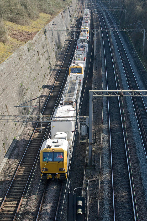 Network Rail HOPS train, 12.03 Chelmsford reception sidings-Crewe MD (11L), Roade cutting 
 One of Network Rail's HOPS trains passes through Roade cutting as the 12.03 Chelmsford to Crewe working. These 40m 'factories on wheels' were built for Network Rail by Windhoff Bahn und Anlagentechnik GmbH, in Germany, for the electrification of the GWML. Unfortunately, they did not speed up this process and were one of the cogs in the debacle that actually delayed it. I hope that those responsible for the procurement of these enormously expensive trains were held to account but I suspect that this was lost in the wider analysis. Network Rail still have a very upbeat page and video on their website making things look so beautifully simple, see..... https://www.networkrail.co.uk/running-the-railway/looking-after-the-railway/our-fleet-machines-and-vehicles/high-output/high-output-plant-system-hops 
 Keywords: Network Rail HOPS train 12.03 Chelmsford reception sidings-Crewe Roade cutting High Output Plant System