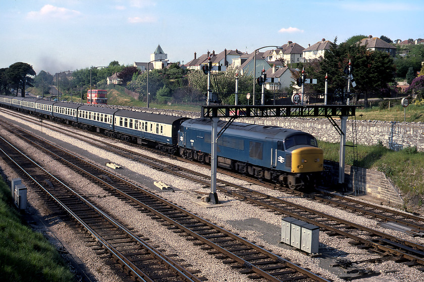 45041, unidentified Paignton working, Aller Junction 
 Not a particularly good photograph of 45041 'Royal Tank Regiment' as it approaches Aller Junction in Devon leading an unidentified Paignton working. I have managed to clip off the rear of the train and it is a little blurred as the weaknesses of the Rollie B35 camera are revealed. Whilst the Peak still carries its nameplate the crest of the Royal Tank Regiment has been removed. The A380 road in the background has now been swept away with a new dual carriageway replacing it with the bridge that I am standing on having been removed to make way for these works. 
 Keywords: 45041 unidentified Paignton working Aller Junction Royal Tank Regiment