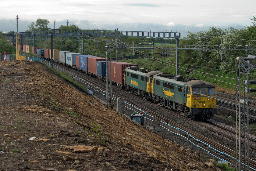 86609 & 86604, 02.50 Felixstowe North-Garston (4M56, 30E), Ashton Road bridge 
 Veteran AC power in the form of 86609 and 86604 lead the 02.50 Felixstowe to Garston 4M56 Freightliner past the worksite at Ashton Road bridge just south of Roade in Northamptonshire. After a foul day yesterday with relentless rain, this day has dawned a little brighter so maybe I can continue with some of my COVID-19 lockdown jobs? 
 Keywords: 86609 86604 02.50 Felixstowe North-Garston 4M56 Ashton Road bridge