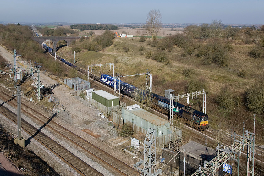 66427, 12.03 DIRFT-Purfleet (4L98), Blisworth Road bridge 
 In decidedly spring-like weather DRS' 66427 hauls the 12.03 Daventry to Purfleet 4L98 up the 1:100 long drag from Northampton to Roade cutting where things level out. Apart from the front few flats being unladen the rest of the train appears well loaded. The line in the foreground is the Weedon route that avoids trains going through Northampton. The town of Northampton can be seen in the background with the town's Express lift tower visible on the skyline centre left. 
 Keywords: 66427 12.03 DIRFT-Purfleet 4L98 Blisworth Road bridge Tesco Express DRS Direct Rail Services