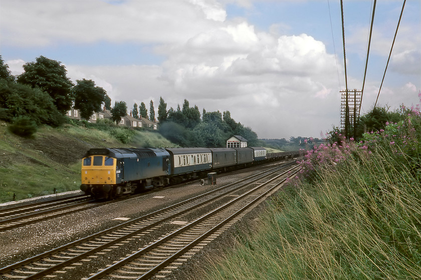 25280, down freight, Kettering Junction 
 25280 trundles along the down slow line at Kettering Junction with a mixed train composed of what appears to be some loaded parcels wagons (judging by their white labels under the spring-loaded clamps) and some flats of some kind. The row of semi-detached houses on Sussex Road on top of the embankment are still there very much the same but their views of the MML are somewhat compromised by rampant tree growth 
 Keywords: 25280 down freight Kettering Junction