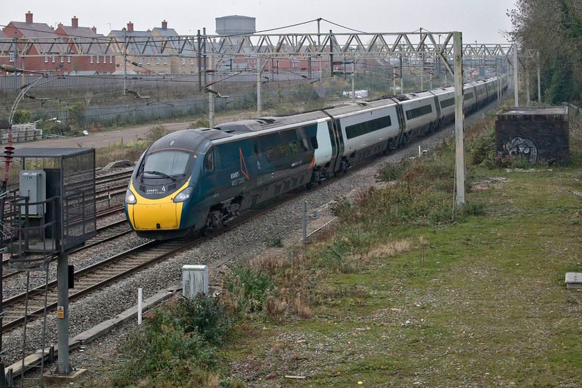 390103, VT 12.17 London Euston-Manchester Piccadilly (1H08, 1E), site of Roade station 
 390103 passes Roade in full-gloom working the 12.17 Euston to Manchester Avanti West Coast service. Close examination of the photograph reveals a mass of hi-viz in the background with a possession of the slow lines in place. This was to facilitate the contractors reconstructing the embankment just north of Ashton Road bridge. 
 Keywords: 390103 12.17 London Euston-Manchester Piccadilly 1H08 site of Roade station Avanti West Coast