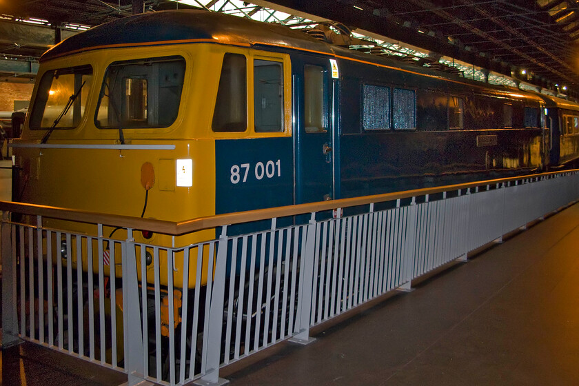 87001, preserved, NRM 
 87001 was the first built of thirty-six members of the class that entered service with BR in 1973 and were the first set locomotives that carried TOPS numbers from new. This rather dark photograph shows the preserved locomotive at the National Railway Museum carrying its 'Stephenson' plates as opposed to the 'Royal Scot' set that it can also be found wearing. 
 Keywords: 87001 preserved NRM National Railway Museum AC electric Stpehneson Royal Scot