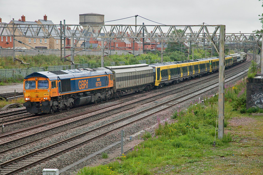 66730, 777005 & 777009, 02.44 Dollands Moor-Kirkdale (6X29, 5L), site of Roade station 
 In the utter gloom of a foul July morning, 66730 'Whitemoor' leads the 02.44 Dollands Moor to Kirkdale new stock movement through Roade. The GBRf locomotive is towing a pair of brand new Merseyrail units to their new home having arrived from the continent through the tunnel the previous day. 777005 and 777009 are the units being conveyed and now several months late with the first ones due in service by now. Notice that the units are articulated following in the best traditions of innovative design such as was applied to the APT-P, the LNER Silver Jubilee train and Eurostars to name just three. There was a very interesting article in Traction issue 257 on the subject of railway articulation written by Colin Boocock. 
 Keywords: 66730 777005 777009 02.44 Dollands Moor-Kirkdale 6X29 site of Roade station Merseyrail Stadler Whitemoor