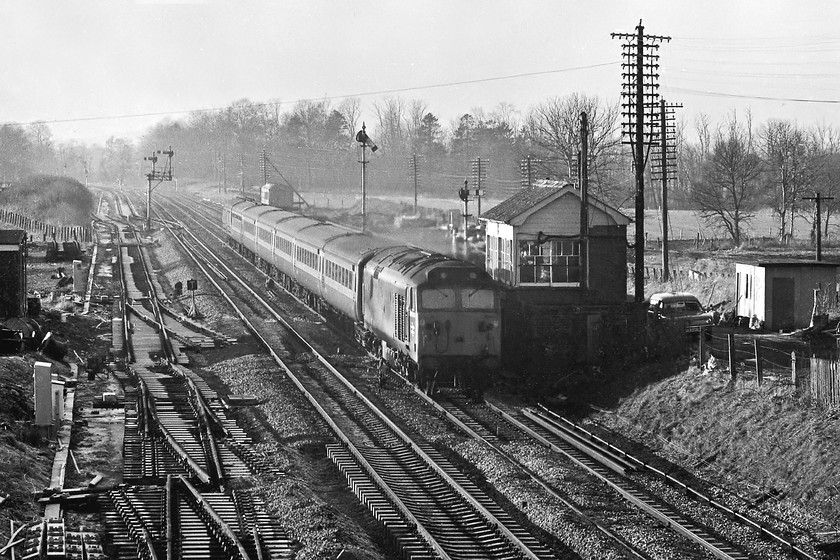 50042, 12.08 Paignton-London Paddington, Woodborough 
 50042 'Triumph' rattles Woodbrough signal box as it passes at speed with the 12.08 Paignton to Paddington. Despite extensive research, I cannot find the reporting number of this train, can anybody help? This is a messy scene at Woodbrough. The track panels laying by the side of the down fast line indicate that there is extensive work taking place. Indeed, the signal box and and mechanical signalling only had another seven days in use as it was all replaced by MAS signalling controlled by Reading PSB the following weekend. Notice the phase one Marina van parked behind the box. BR had thousands of these all painted in yellow, this one was probably being driven by an S & T technician attending the box rather than belonging to the signalman. 
 Keywords: 50042 12.08 Paignton-London Paddington Woodborough