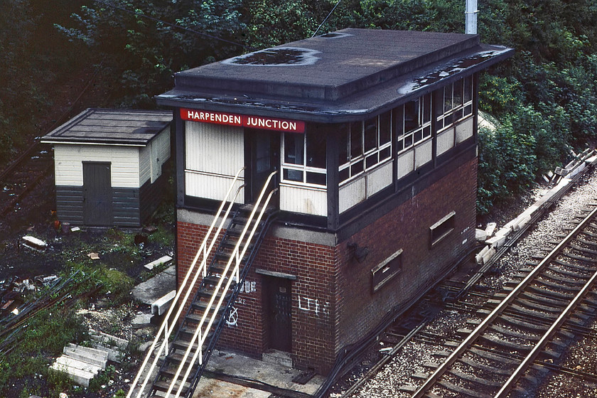 Harpenden Junction signal box (BR, 1957) 
 Harpenden Junction signal box is viewed from Hollybush Lane bridge. This 1957 built box was a standard British railways design with its flat roof complete with a pool of water! Behind the box is the remains of the track leading to Hemel Hempstead referred to as the Nickey Line. The line was in the throes of complete closure as its remaining use to carry flyash to the Hemelite Company at Cupid Green had ceased. Soon the track was removed and the trackbed was acquired by St. Albans District Council and Dacorum Borough Council. It was turned into a cycle and footpath and is now an extremely popular local resource, see.... http://www.nickeyline.org/home/ I visited this spot again in 2023 and took a very similar photograph, see.... https://www.ontheupfast.com/p/21936chg/30041562429/x3-site-harpenden-junction 
 Keywords: Harpenden Junction signal box