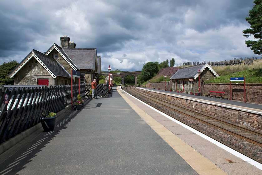 Dent station 
 Some summer sunshine brightens the scene at Dent station. Andy is seen taking a photograph of the large wooden sign just out of shot proclaiming that the station is the highest in England at one thousand one hundred and fifty feet. The station reopened back in 1986 along with many others on this dramatic and scenic line mainly for tourists as, in this case, the station is somewhat divorced from any settlement. The station building has been used for holiday accommodation that unfortunately, my wife seemed singularly uninterested in renting out for a week when I told her all about it; I can't understand why? 
 Keywords: Dent station