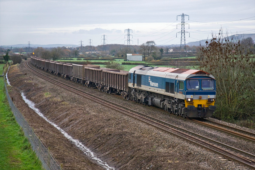 Class 59, 13.34 Exeter Riverside-Whatley Quarry, Berkley ST806498 
 An unidentified Class 59 heads past Berkely between Frome and Westbury leading the 13.34 Exeter Riverside to Whatley empty stone train. Appearing to be running the wrong way the train will initially have worked past this spot heading east as far as Westbury where it will have reversed to head west again allowing access to the Whatley branch. This well know spot has been completely opened up to the railway photographer due to drainage work undertaken necessitating complete clearance of the extensive and uncontrolled lineside vegetation. It is also pleasing to see that Network Rail has replaced the fencing with a standard type rather than instaling the hideous and totally unnecessary palisade type.....where's my tin hat gone? If anybody can assist with the identification of this Class 59 I would appreciate it. 
 Keywords: Class 59 13.34 Exeter Riverside-Whatley Quarry Berkley ST806498 Hanson Rail