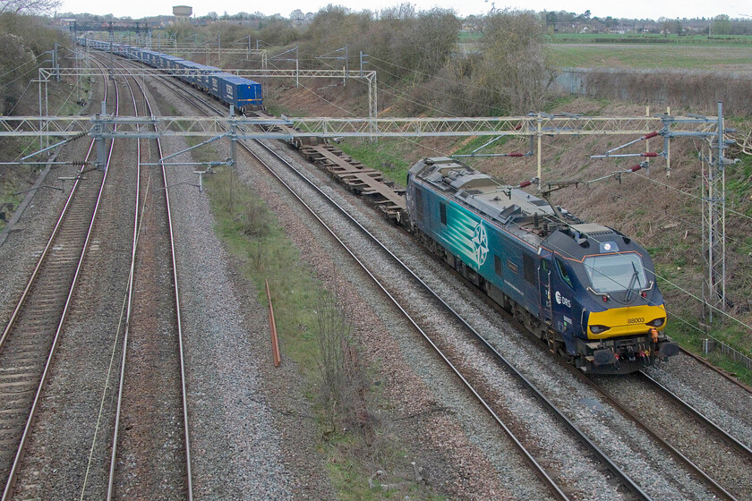 88003, 13.37 DIRFT-Tilbury (4L48, 100L), Victoria bridge 
 Running extremely late having left DIRFT well over two hours after it should have done the driver of 88003 Genesis will have the power handle pulled back eager to make up some lost time. Indeed, the speed that the fully loaded (apart from a few spaces at the front) 4L48 Tesco Express from DIRFT to Tilbury docks made it from Northampton to this spot at Victoria bridge a few miles south was remarkable; I would suggest that it was twice as quick as a Class 66 would do it on the steady rising gradient all the way. 88003 was a photographic cop, they are never particularly common south of DIRFT as they are to the north. 
 Keywords: 88003 13.37 DIRFT-Tilbury 4L48 Victoria bridge Genesis