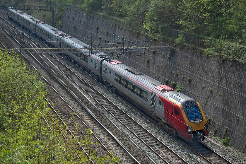 221103, VT 11.30 London Euston-Chester (1D85, RT), Roade cutting 
 For all intents and purposes, this still appears to be a fully-fledged Virgin working passing through Roade cutting some five months after the operator handed over the reins to Avanti West Coast! 221103 'Christopher Columbus' works the 11.30 Euston to Chester 1D85 service no doubt with very few passengers on-board due to the COVID-19 crisis that has enveloped the country (and the world for that matter). 
 Keywords: 221103 11.30 London Euston-Chester 1D85 Roade cutting Virgin Avanti West Coast Voyager