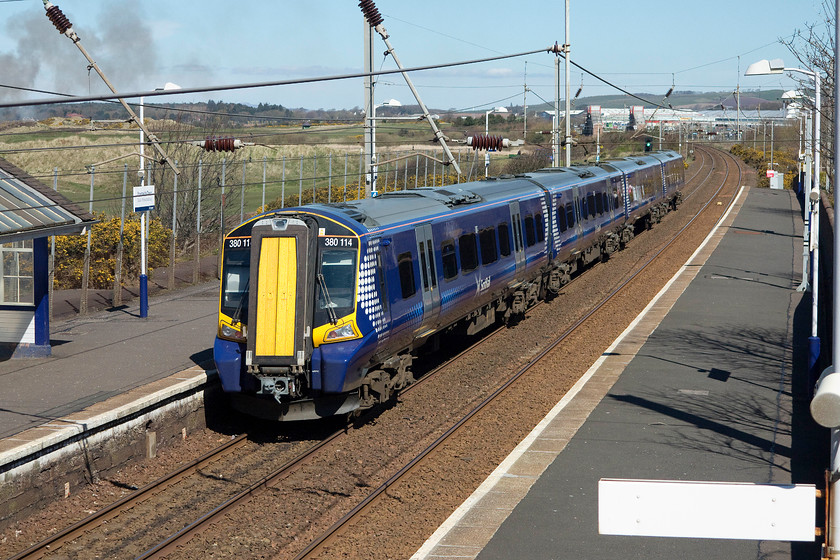 380114, SR 11.52 Ayr-Glasgow Central (1K28), Prestwick Town station 
 Having arrived at Prestwick Town, I turned my camera round to capture 380114 leaving with the 11.52 Ayr to Glasgow Central. In the background, the buildings of Prestwick Airport can be clearly seen. This has its own station opened in 1994 and remains Scotland's only station that is directly linked to an airport facility. I am not sure what the black smoke drifting in from the left was, but its originating from somewhere on Troon Golf Club. 
 Keywords: 380114 11.52 Ayr-Glasgow Central 1K28 Prestwick Town station