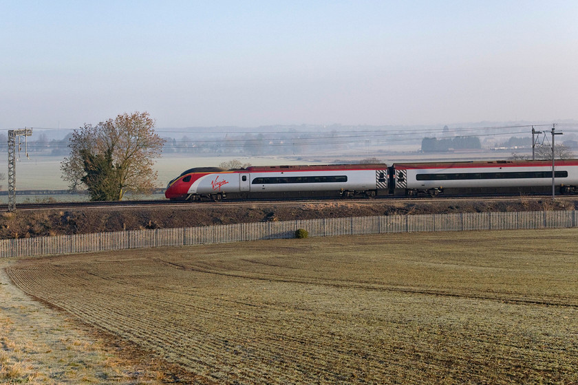 Class 390, VT 07.23 London Euston-Birmingham New Street (1G05), Blisworth 
 The 07.23 Euston to Birmingham New Street Pendolino services passes through the cold Northamptonshire countryside. This location is just outside the village of Blisworth in a field adjacent to the village's football club pitches. Shrouded by the mist in the background is the county town of Northampton with the National (formally the Express) lift tower just visible catching the rising sun on the extreme right. 
 Keywords: Class 390 07.23 London Euston-Birmingham New Street 1G05 Blisworth Virgin Trains Pendolino