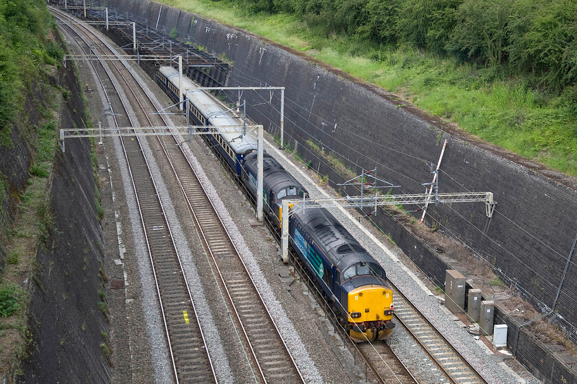 37605 & 37602, 13.44 London Euston-Crewe HS ECS (5Z28), Roade cutting 
 Dead in tow on the rear of the 13.44 Euston to Crewe HS 5Z28 empty stock working 37605 and 37602 are dragged through Roade cutting. The Class 37s and the stock had been operating The Three Peaks Challenge charity train over the last few days venturing to North Wales, Cumbria and the west coast of Scotland. I saw the outward leg a few days previously but this time I escaped uninjured from my trip out, see.... https://www.ontheupfast.com/default.asp 
 Keywords: 37605 37602 13.44 London Euston-Crewe HS ECS 5Z28 Roade cutting DRS