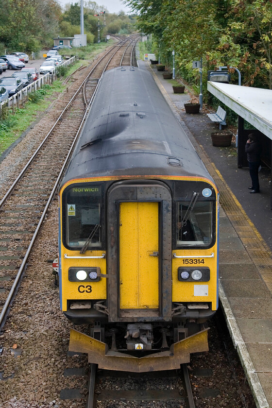 153314, LE 12.17 Great Yarmouth-Norwich, Brundall station 
 Having alighted from 153314 at Brundall I have nipped up on to the footbridge to capture its departure from this quiet East Anglian station. Notice the single up platform with the down platform located behind me on the other side of the bridge and a level crossing. 
 Keywords: 153314 12.17 Great Yarmouth-Norwich Brundall station Greater Anglia