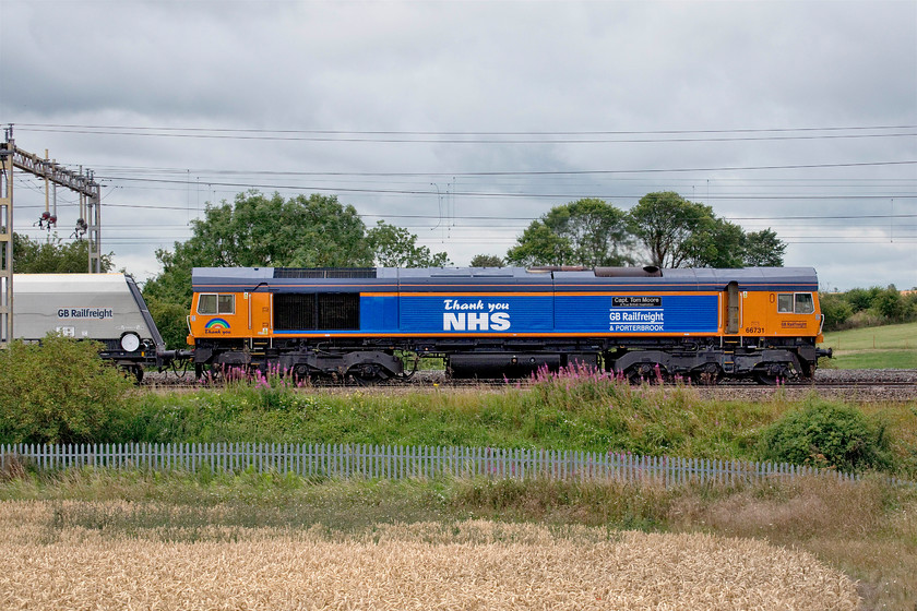 66731, 10.55 Bletchley Cemex-Peak Forest (4H04, 5E), between Roade & Ashton 
 I have been attempting to get a photograph of celebrity 66731 'Capt. Tom Moore A True British Inspiration' since its naming deep in the depths of the pandemic lockdown on 30.04.20. This broadside photograph shows the various other adornments applied to the side of what is an otherwise mundane Class 66 that makes it stand out from the crowd. 66731 is hauling the 10.55 Bletchley to Peak Forest empty stone train diverted away from its usual route down the MML seen between Ashton and Roade on the WCML. 
 Keywords: 66731 10.55 Bletchley Cemex-Peak Forest 4H04 between Roade & Ashton Capt. Tom Moore A True Inspiration Thank You NHS GNRf