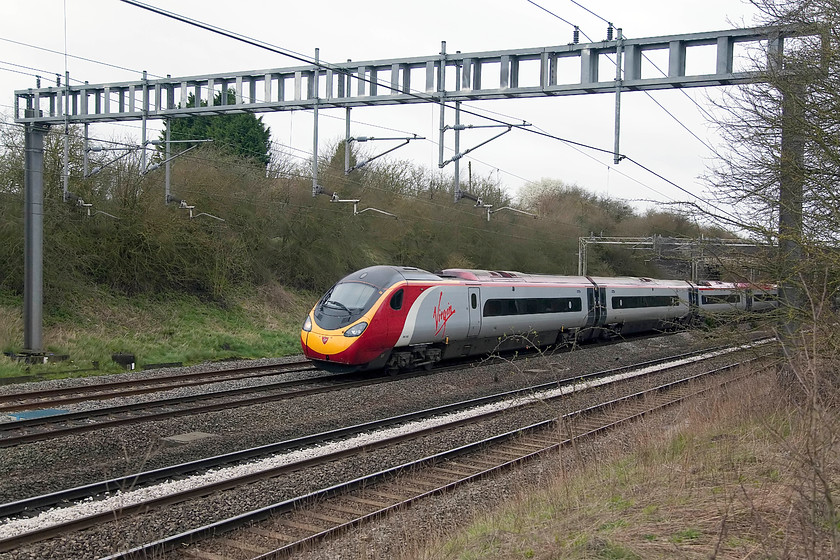 390043, VT 06.10 Manchester Piccadilly-London Euston (1A05, 2E), Ashton Road bridge 
 VT's 390043 heads south past Ashton Road bridge near Roade working the 06.10 Manchester Piccadilly to London Euston. Since the palisade fencing was installed at this location photography has been compromised somewhat. A ladder helps but there is a cut-off telegraph pole that can be stood on for taking down trains. 
 Keywords: 390043 1A05 Ashton Road Bridge