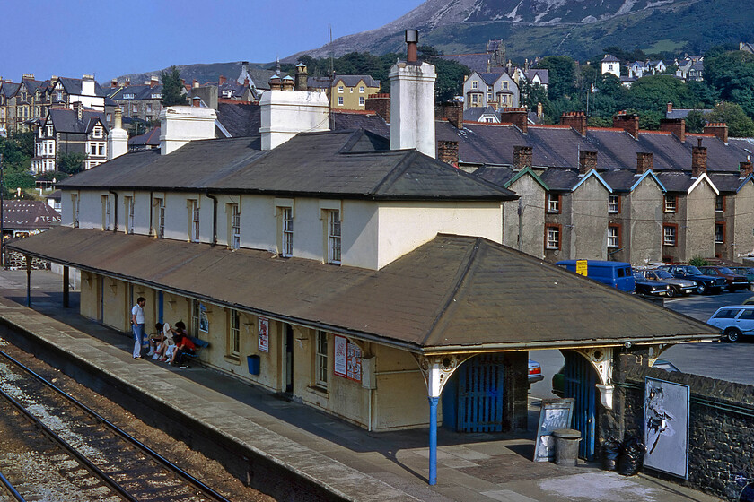 Penmaenmawr station 
 A family sit in the afternoon shade under Penmaenmawr station's canopy waiting for their train on this hot Sunday afternoon. The station opened in 1849 with the building now Grade II listed and has undergone a sensitive restoration in the hands of its new private owner. Notice the cars of the era parked behind the station including a Chevette, a Marina, the inevitable Cortina and a Volvo with the rear of a Morris Ital (the reworked Morris Marina) seen through the station gate. I last visited the station in 2016 with Andy, see.... https://www.ontheupfast.com/p/21936chg/25632547804/penmaemawr-station 
 Keywords: Penmaenmawr station