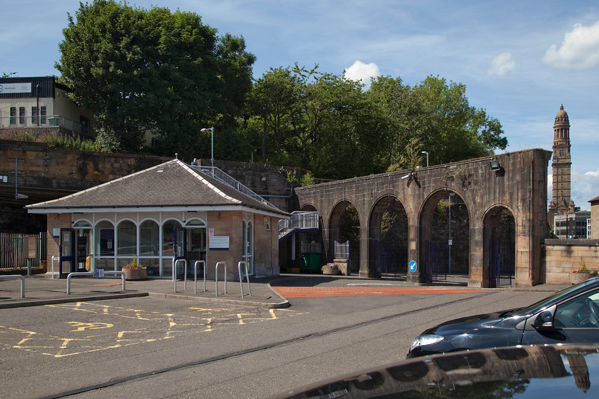 Frontage, Greenock Central station 
 At least Greenock Central station has a ticket office! Having been re-built and had a far more appropriate hipped roof added the facilities remain basic. All the remains of this once quite grand station is the tall wall with the arches. This used to be the front of the building with the arches upper halves being glazed and with the lower halves having the doors into the booking hall. Today, they have to be driven through to get into the car park and a little tight they are too with evidence of contact with a number of vehicles at the sides! In the background, Victoria Tower can be seen towering above Greenock Town Hall. 
 Keywords: Frontage Greenock Central station