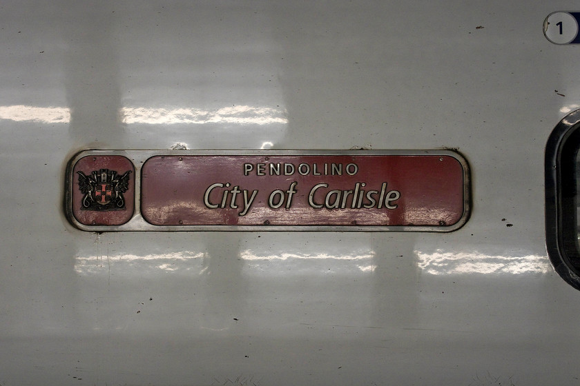 Nameplate, 390034, VT 19.30 London Euston-Glasgow Central (1S06, 3L), London Euston station 
 As Virgin work through the Pendolino fleet turning them out in their new flying silk livery these traditional cast nameplates are removed. They are not reunited with the trains but alternative vinyls are stuck on to the bodysides. This seems a shame as the cast plates maintain a tradition of naming trains properly and making a statement about their identity. I wonder what is happening to the old cast plates? Here at Euston, 390034 'City of Carlisle' waits to leave with the 19.30 to Glasgow Central. 
 Keywords: Nameplate 390034 1S06 London Euston station