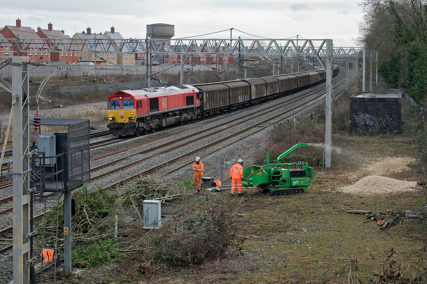 66130, 06.53 Dollands Moor-DIRFT (6M45, RT) & trackworkers, site of Roade station 
 With one load of cleared vegetation and trees having been cut and then carried back to this worksite in Roade, contractors are now chipping and stacking the logs. This type of work can only be carried out at certain times so as to protect birds and other small nesting animals after a survey has been undertaken. Whilst this may seem a little over onerous if the embankments were managed better in the first place not allowing them to get so grossly overgrown it would not be an issue. 66130 passes heading north with the 6M45 06.53 Dollands Moor to Daventry bottled water train. 
 Keywords: 66130 06.53 Dollands Moor-DIRFT 6M45 trackworkers site of Roade station DB