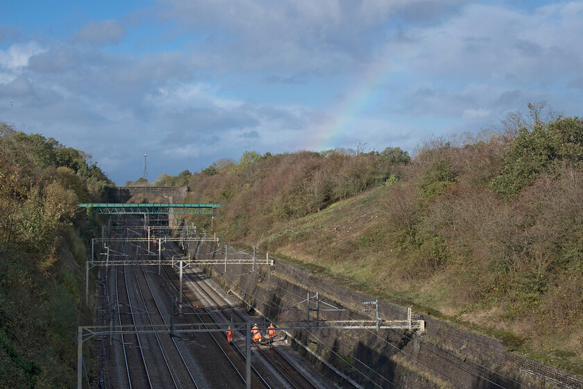 Track inspection & rainbow, Roade cutting 
 With a chainsaw, some fuel and a billhook a group of track workers head very slowly along the line through Roade cutting carrying out an inspection of the lines paying particular attention to fallen trees or branches. I do not understand why they are on the slow lines and headed off along these tracks as these were clear with two engineering trains having traversed them a little earlier? I bet that the workers did not spot the lovely rainbow above them from the depths of the cutting! 
 Keywords: Track inspection rainbow Roade cutting