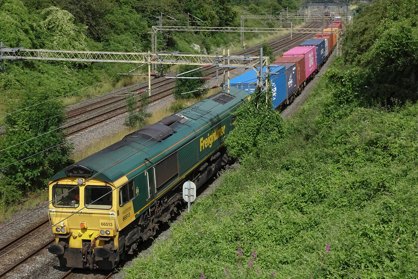 66513, 06.15 Trafford Park-London Gateway (4L44, 13L),Victoria bridge 
 A photograph that amply illustrates the rampant lineside growth taking place at Victoria bridge just south of Roade. Indeed, while at the bridge the gathered enthusiasts attracted the attention of a Network Rail employee doing his rounds. He was also concerned about the growth of bindweed that was totally encroaching on various masts. We also pointed out the small ash trees that have started to become a problem between the slow and fast lines seen to the left of the train. 66513 leads the 06.15 Trafford Park to London Gateway passes the scene. 
 Keywords: 66513 06.15 Trafford Park-London Gateway 4L44 Victoria bridge Freightliner