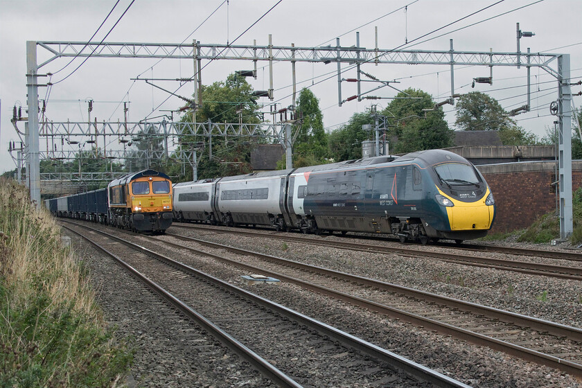 66757, 09.15 Tunstead-Northampton Castle Yard (6B92, 15L) & 390050, VT 12.55 Manchester Piccadilly-London Euston (1A35, 5E), Madeley SJ773439 
 The race is on! At Madeley just south of Crewe GBRfs 66757 West Somerset Railway leads the 09.15 Tunstead to Northampton Castle Yard loaded stone train whilst the 12.55 Manchester Piccadilly to Euston Avanti service passes it on the up fast line worked by 390050. It is tricky locations such as this where the cameras flip-out screen is absolutely invaluable with me able to poke the camera through the palisade fencing to secure an interesting photograph. 
 Keywords: 66757 09.15 Tunstead-Northampton Castle Yard 6B92 390050 12.55 Manchester Piccadilly-London Euston 1A35 Madeley SJ773439 GBRF Avanti West Coast Pendolino West Somerset Railway