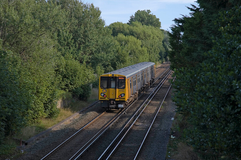 507010, ME 17.48 Southport-Liverpool Central, Hightown 
 The 17.48 Southport to Liverpool Central service worked by 507010 catches some evening sunshine between some tall trees as it leaves Hightown. 
 Keywords: 507010 17.48 Southport-Liverpool Central, Hightown Merseyrail