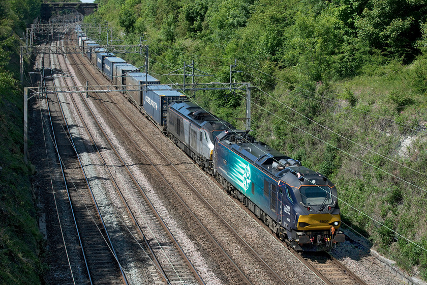 88005 & 68015, 14.20 DIRFT-Mossend (4Z45, 9E), Hyde Roade bridge 
 In glorious late-spring sunshine, which is unusual as it's a Bank Holiday weekend, 88005 'Minerva' leads 68015 through Roade cutting taken from Hyde Road bridge. The 4Z45 14.20 Daventry to Mossend 'Tesco Express', as it is dubbed, is on a lengthy diversion running south to London, then taking to heading north again on the ECML adding considerable mileage to its journey. Whilst the Class 88 is in DRS Compass livery the Class 68 is one of Chiltern's that are leased from DRS. These services have all had a diesel tucked in behind the leading electric so I wonder if there is part of the journey where the overhead power is switched off for engineering works...advice anybody?

I have been advised by my spotting companion Mike that the Class 68 is in the consist due to power supply issues in the northeast. When this diversion ran last week the working timetable was much reduced so there was less of a demand on available power that could be supplied from the catenary but now that traffic has increased to around 75% the diesel is used to ease the train through the troublesome areas that Network Rail have yet to upgrade. 
 Keywords: 88005 68015 14.20 DIRFT-Mossend 4Z45 Hyde Roade bridge DRS Direct Rail Services Tesco Express Minerva