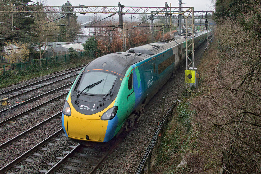 390121, VT 09.43 London Euston-Liverpool Lime Street (1F16, 6L), Apsley 
 The one-off livery applied to 390121 'Opportunity' certainly brightens up the otherwise dull and damp winter scene at Apsley. The Pendolino is working the 09.43 Euston to Liverpool Street Avanti West Coast service. I was quite impressed with the photographic opportunities at this location with the bridge suitably free of restricting anti-suicide extensions but the light is tricky. Even on a bright day, a huge line of tall trees to the right in this view would prevent any trains from being in the sun. 
 Keywords: Opportunity 390121 09.43 London Euston-Liverpool Lime Street 1F16 Apsley AVWC Avanti West Coast