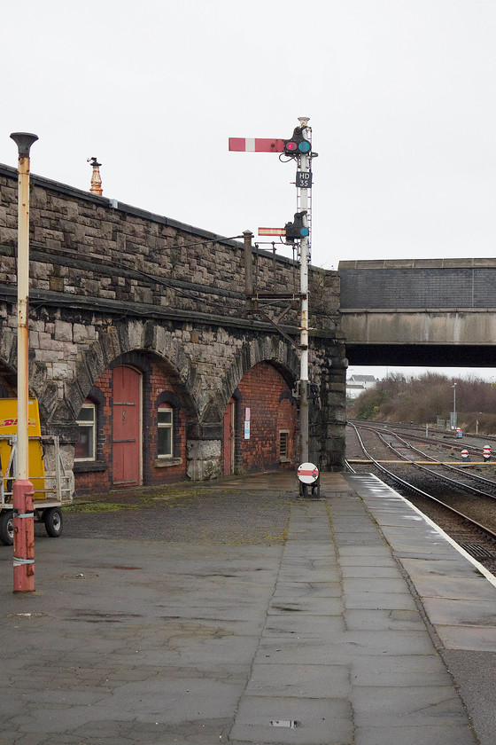 Up starter signal, platform 1, Holyhead station 
 Holyhead station's platform one starter signal is seen along with a number of other mechanical signals. The signal post has a permissive calling-on arm below the main arm. This allows a driver to pass the main arm at danger in order to complete a move, for example for an engine to be released from its train. Above the substantial stone wall is the station access road that leads to the bridge that marks the start of the main A55 trunk road. 
 Keywords: Up starter signal platform 1 Holyhead station