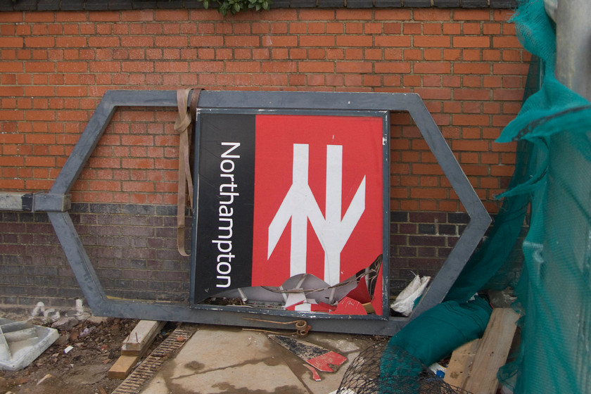 Old station sign, Northampton station 
 The old station sign lies ignominiously on its side and badly broken ready for removal from the worksite where the new station is being constructed at Northampton. It would have been nice to have saved the sign and preserve it. Maybe not now, but in many years to come, this style of sign may well have the same collection value as enamels or even totems from the early British Railways days do now! 
 Keywords: Old station sign Northampton station