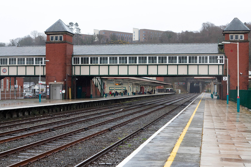 Bangor station 
 During my last visit to Bangor in August 1981 (apart from being hospitalised at Ysbyty Gwynedd in July 1989!) I took an almost identical picture to this. It shows the footbridge and lift towers with things look very similar, see..... https://www.ontheupfast.com/p/21936chg/30035069793/x36-bangor-station. The platforms to the right of the green fencing have now gone and the university buildings on top of the hill have been rebuilt. The station appeared to be in very good condition and was well used, indeed its passenger numbers have begun to rise again. 
 Keywords: Bangor station