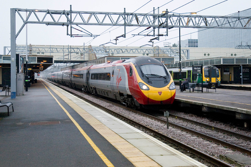 Class 390, VT 07.46 Carlisle-London Euston (1M07) & 350250, LM 09.14 Birmingham New Street-London Euston (1Y22), Milton Keynes Central station 
 As this class 390 Pendolino was not stopping at Milton Keynes it was passing through at full line speed this made it impossible to identify its number. It was working the 1M07 07.46 Carlisle to Euston. To its right, 350250 is waiting to leave forming the 1Y22 09.14 Birmingham New Street to Euston. 
 Keywords: Class 390 07.46 Carlisle-London Euston 1M07 350250 09.14 Birmingham New Street-London Euston 1Y22 Milton Keynes Central station