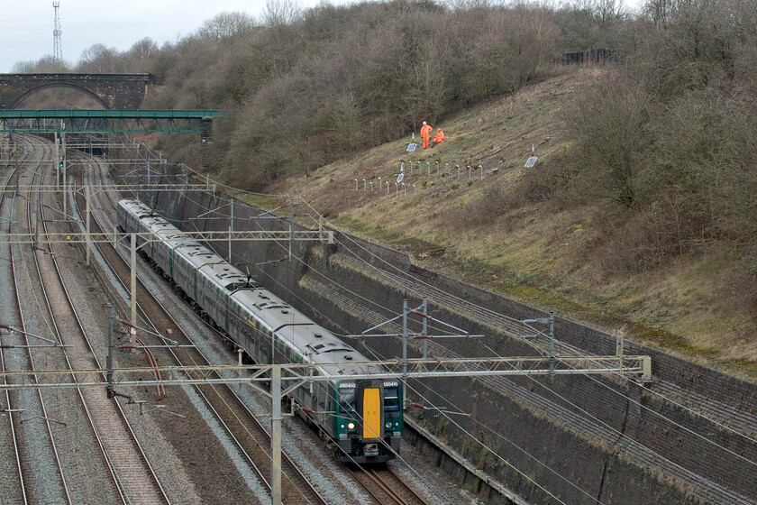 350410, LN 12.25 Northampton-London Euston (1Y20, 1L), Roade cutting 
 Further work continues in Roade cutting as preparations for the new bridge that will be constructed to carry Roade's much-needed bypass across the railway. I spoke with the two Network Rail employees and they told me that the solar panels are providing electrical power to the movement monitors that have been installed where the bridge will be constructed amid constant concerns about the stability of the cutting walls and slopes. I also quizzed them about the design of the bridge with no published detail yet available. They said that they had seen the plans and that it will be a stained naturally resisting steel structure rather than one of the more favoured green monstrosities that seem all too common. 350410 leads another unit through the cutting working the 1Y20 12.25 Northampton to Euston service. 
 Keywords: 350410 12.25 Northampton-London Euston 1Y20 Roade cutting London North Western Desiro