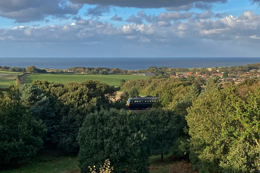 E51188, 16.35 Holt-Sheringham, Kelling Heath 
 On arrival back at our base for the week on Kelling Heath my wife and went for a stroll to take in the late afternoon views. As we were looking across to the North Sea and Weybourne the final train of the North Norfolk Railway's timetable slipped quietly downhill through the trees below us. This shows the trailing car of one of the NNR's two Class 101 DMU sets just being picked out by the last vestiges of sunshine reaching into the woods below. 
 Keywords: E51188 16.35 Holt-Sheringham Kelling Heath Class 101 DMU