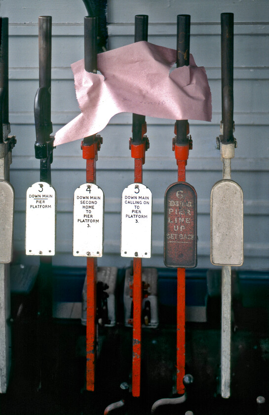 Levers, New Holland Town signal box 
 With work already underway in preparation for the closure of New Holland Town station and signal box in a week's time (24.06.81) rather crude alterations to the workings of the box are seen in this photograph. Possibly in lieu of a piece of red paper, a pink sheet of A4 has crudely been placed across some levers to remind the signalmen not to use them. Notice that standards have appeared to have slipped a little with regard to the handles of the levers that normally would be highly polished but look distinctly tarnished. 
 Keywords: Levers New Holland Town signal box