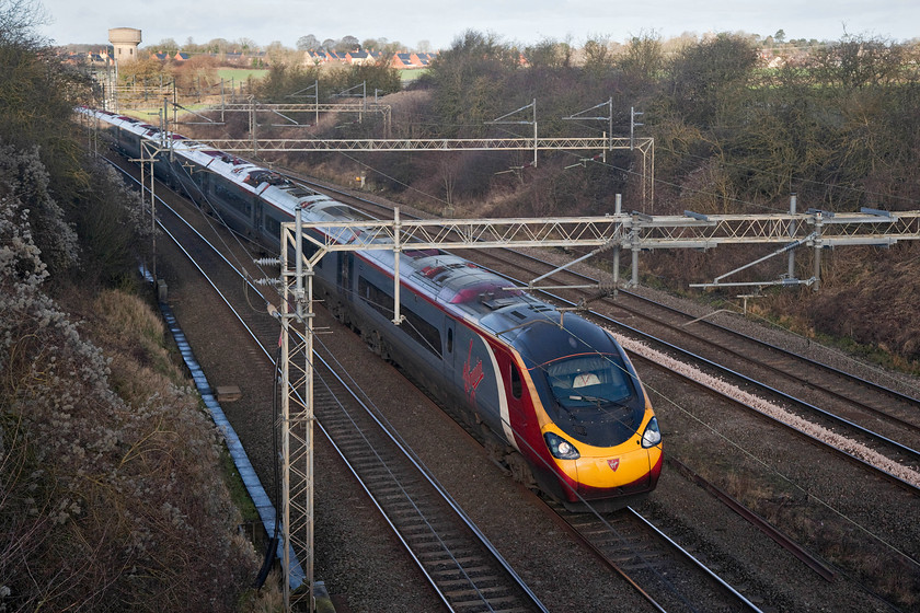 390117, VT 06.30 Glasgow C-London Euston (1M07, 15L), Victoria Bridge 
 390117 'Virgin Prince' races past Victoria Bridge forming the 06.30 Glasgow Central to London Euston running as 1M07. This is the second up working of the day to leave Glasgow (excluding the sleepers) but the first to reach this far south and is now into the final thirty minutes of its journey. Note the disused Roade water tower in the background and the vast new housing estate that occupies the site of the old Pianoforte factory site. 
 Keywords: 390117 1M07 Victoria Bridge WCML Roade