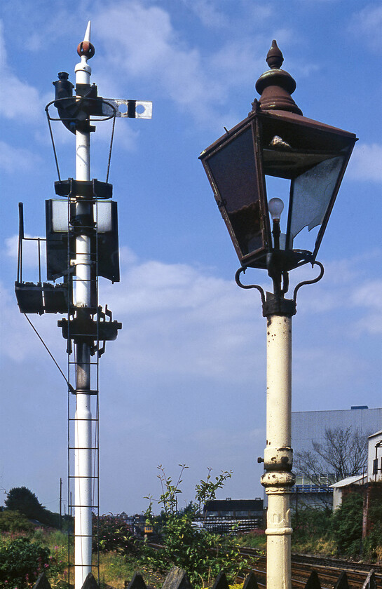 GWR backing signal & converted gas lamp, Croesnewydd North Fork crossing 
 Opposite Croesnewydd North Fork signal box (Wrexham) where these fine pair of GWR antiquities. First is the GWR backing signal with its associated route indicator. This permitted access to sidings to the south of the level crossing on which I am standing. These quirky signals were another type of signal used, primarily by the GWR, to help with special movements. Backing signals were placed to authorise wrong line running at stations or junctions with caution if a ground or subsidiary signal did not cover the movement. The second thing of interest in the photograph is the converted gas lamp. I am not sure of the lamp's origins but it would have been one of possibly three others located on the level crossing where Watery Road crosses the line south of Wrexham station that can be seen in the distance with a DMU in a platform. 
 Keywords: GWR backing signal converted gas lamp Croesnewydd North Fork crossing