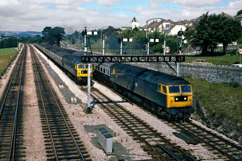 47060, 10.55 London Paddington-Newquay (1B60) & 47129, unidentified Paignton working, Aller Junction 
 The attack of the Duffs at Aller Junction! 47129 has the road on the down Paignton with an unidentified service composed of Mk. 1 stock. Meanwhile, 47060 is being held at the gantry waiting for the road to get the 10.55 Paddington to Newquay away. It is unfortunate that the route is not pegged meaning that the driver will have to make a standing start get away with the line almost immediately beginning its climb of the fearsome but fairly short Dainton bank. By pure coincidence, both these locomotives are still registered and see regular use on the network being owned and operated by DRS. Indeed, 47129 became 47813 and attracted particular attention during the COVID pandemic emblazoned with a large NHS logo, see..... https://www.ontheupfast.com/p/21936chg/29133975204/x47813-11-05-wolverton-centre-sidings 47060 became 57008 in 1999 as one of Freightliner's locomotives. Notice the Mk. 1 Morris Marina racing the train along the A380 road that is painted in one of British Leyland's finest colours 'Harvest Gold' an incredibly optimistic euphemism for beige!

There is an audio recording of this event on my youtube channel, see..... https://youtu.be/26Lvlm6_fs0 
 Keywords: 47129 10.55 London Paddington-Newquay 1B60 47060 Paignton working Aller Junction