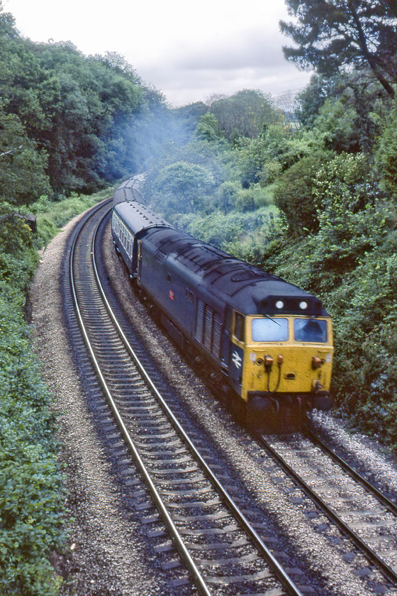 50029, 16.15 St. Austell-Kensington Olympia Motorail (1M01), Wrigwell Bridge Dainton 
 50029 'Renown' approaches the summit of Dainton bank from Wigwell bridge. It is leading the 16.15 St. Austell to Kensington Olympia Motorail service. Unfortunately, due to the curvature of the line, I have not been able to capture the Motorail flats marshalled, as always, at the rear of the train. With the weather having completely clouded over again, and being early evening it was time to turn the Morris 1100 home! 
 Keywords: 50029 16.15 St. Austell-Kensington Olympia Motorail 1M01 Wrigwell Bridge Dainton Renown