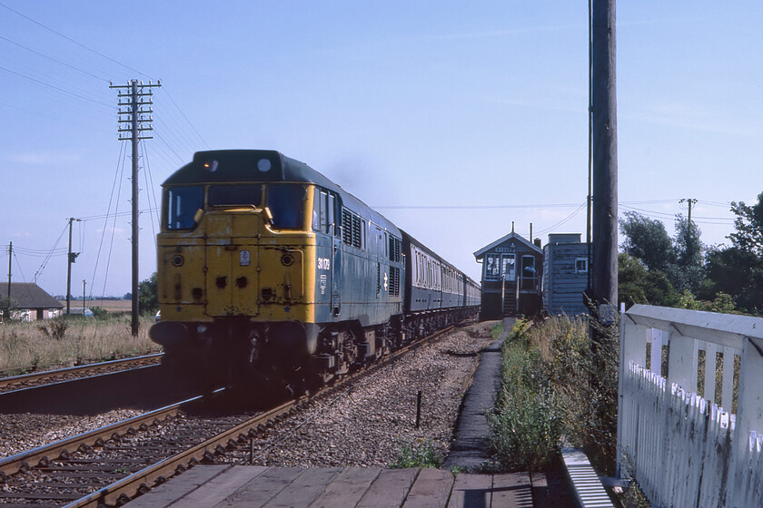 31179, 13.22 Norwich-Birmingham New Street (1M67), Stonea 
 31179 passes Stonea a short distance southeast of March leading the 1M67 13.22 Norwich to Birmingham New Street service. Back in 1981 this was a locomotive-hauled service composed of a long rake of Mk.I stock, today, whilst this exact service does not run parts of it do finding you travelling on either a Class 170 or a Class 158 both composed of just two carriages.progress, Im not so sure? Taken from the safety of the level crossing this signal box can be seen at a jaunty angle caused by it falling into the Fenland soil, two years later it was demolished and replaced with a Portakabin in the same spot. 
 Keywords: 31179 13.22 Norwich-Birmingham New Street 1M67 Stonea